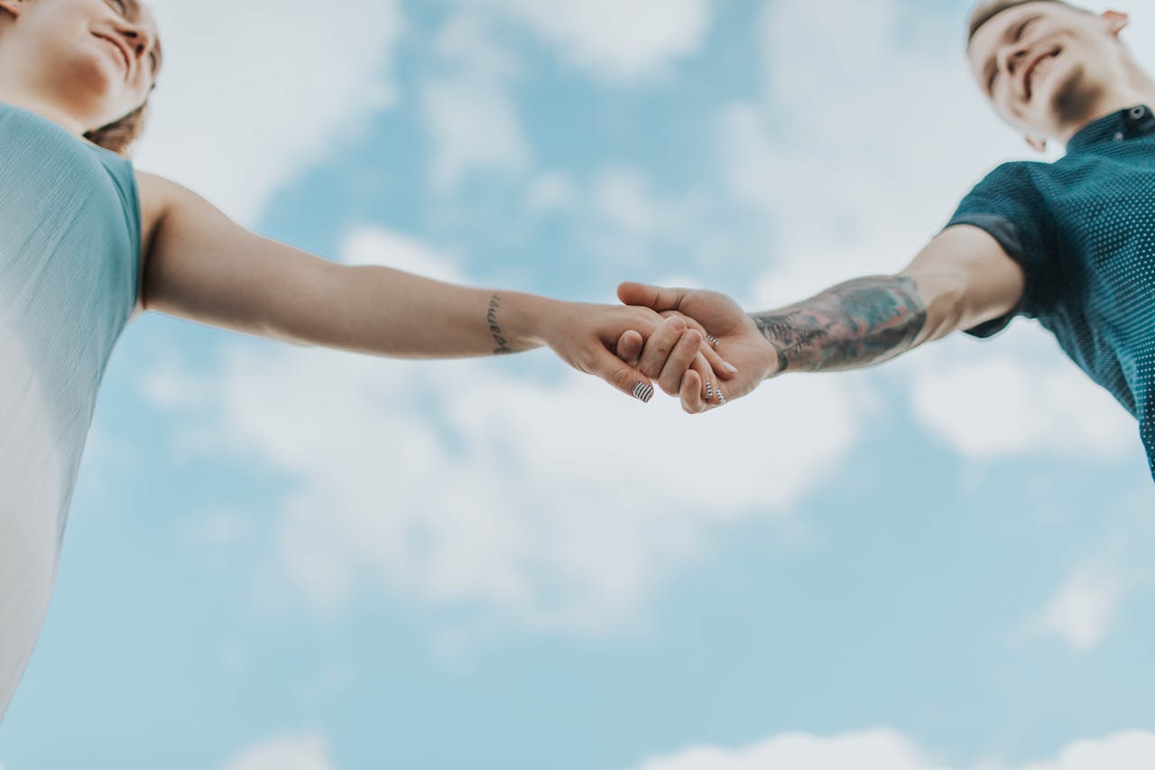 contact A couple holds hands outdoors, symbolizing love and connection, photographed from a low angle.